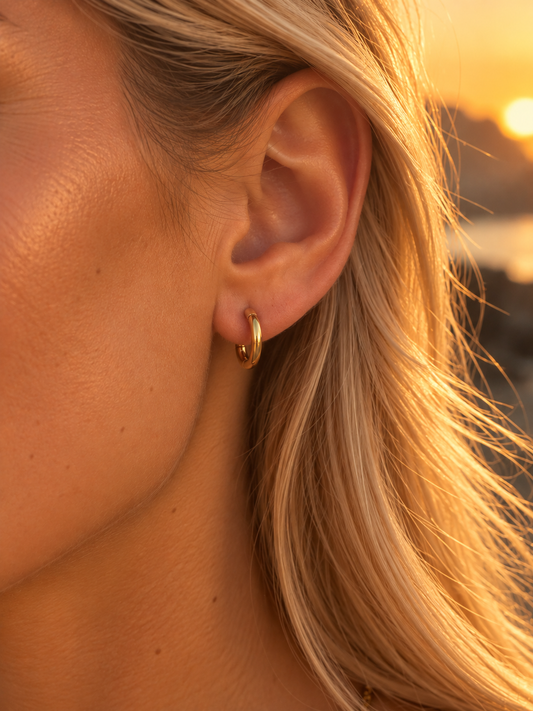 Boucle d'oreille créole dorée Louise en acier inoxydable portée par une femme au coucher du soleil